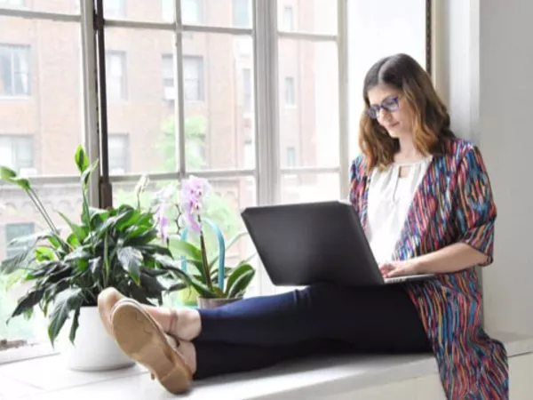 Woman sitting in a window seat, using her laptop to avoid Craiglist scams online.
