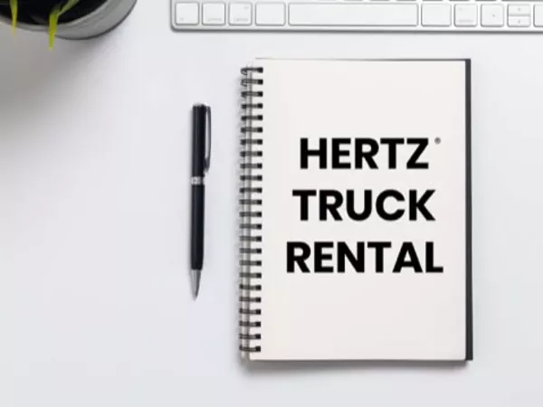 Notepad saying &quot;Hertz Truck Rental&quot; on white table next to keyboard and pen.