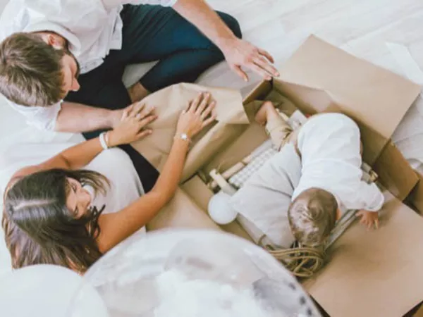 Family packing towels for a move while a baby crawls into the box.
