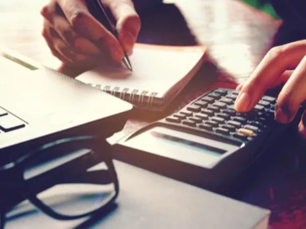 Person figuring out portable storage costs with a laptop, calculator and paper.