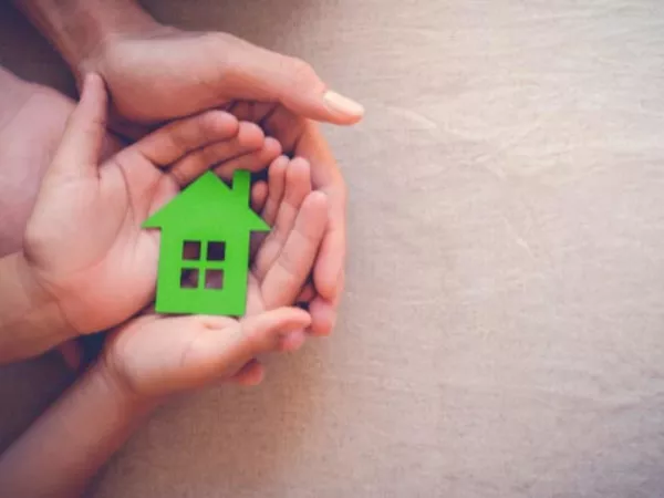 Family holding a green paper house in their hands while planning a moving budget.