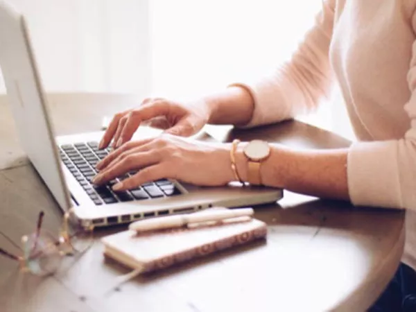 Woman's hands working on a laptop, using paper and pen to understand her moving quote.