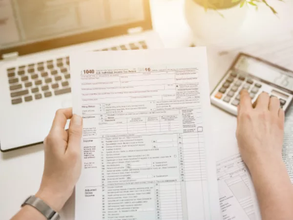 Hands holding an income tax return form and using a calculator to determine deductions.