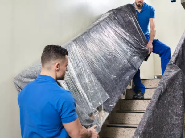 Two hired movers taking a sofa downstairs to load into a moving truck