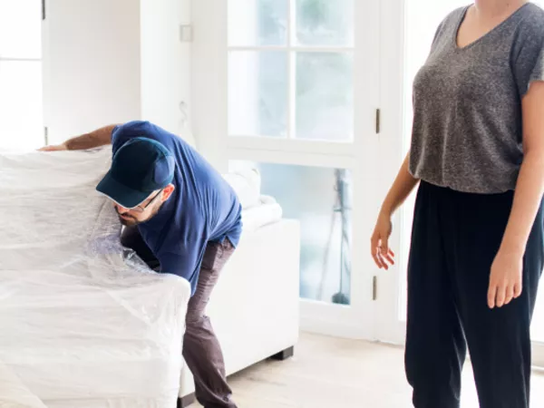 A woman watches two movers pick up her sofa