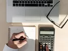 Person figuring the cheapest way to move with a calculator, laptop and paper.