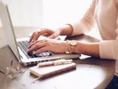 Image of a woman's hands working on a laptop, using paper and pen to understand her moving quote.
